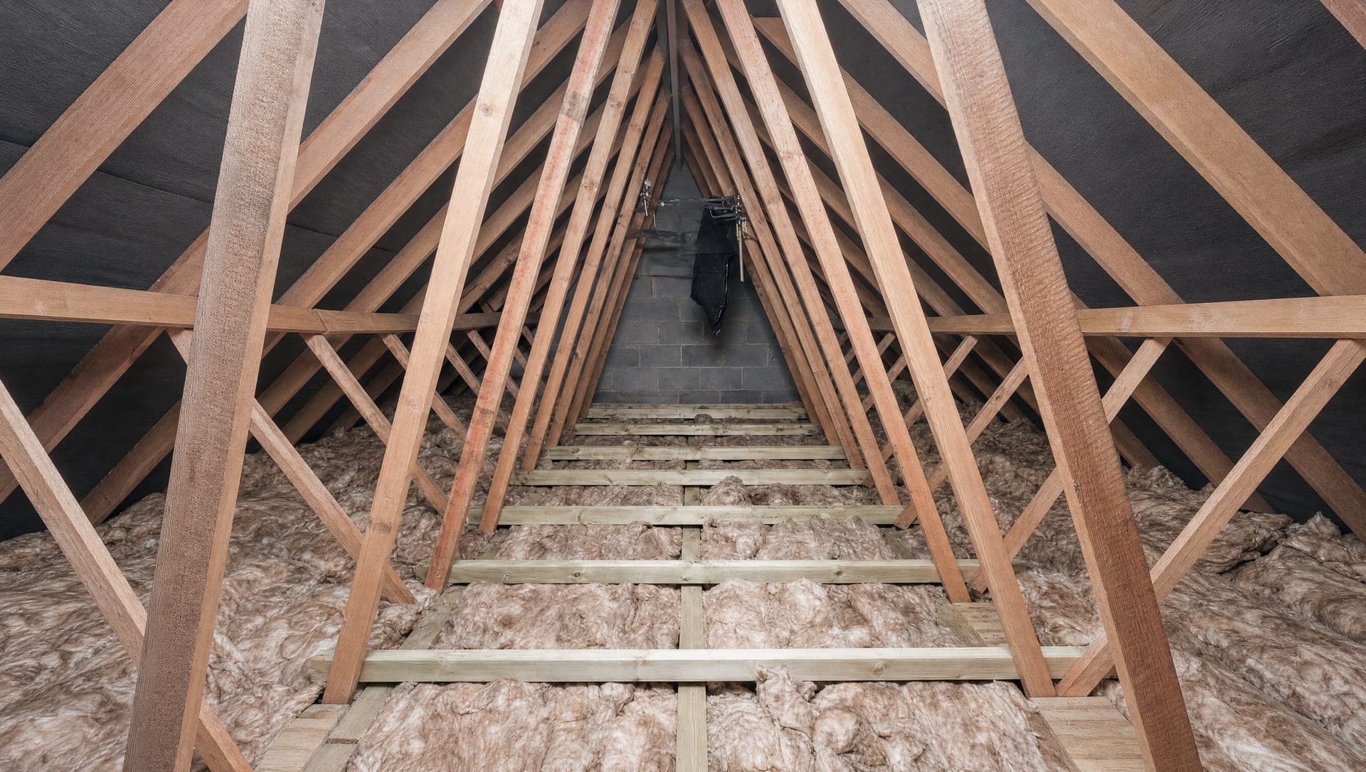 Empty loft viewed end-on with old fibreglass insulation laid loose between joists and no floor