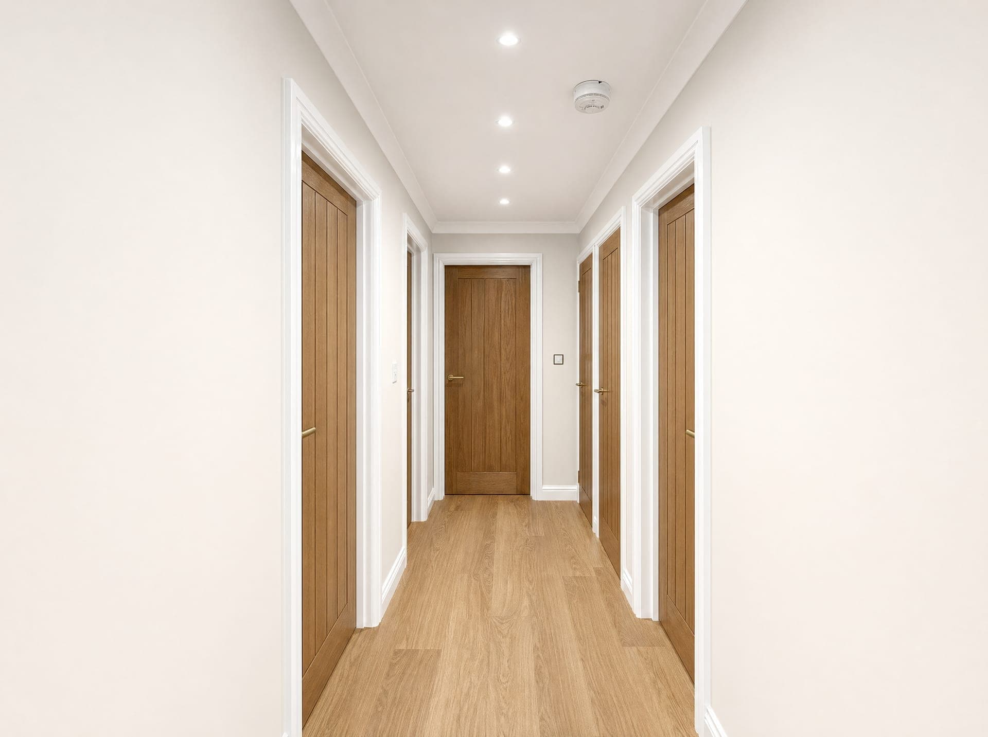 Hallway with multiple oak panelled doors, white architraves, recessed downlights and wood-effect flooring