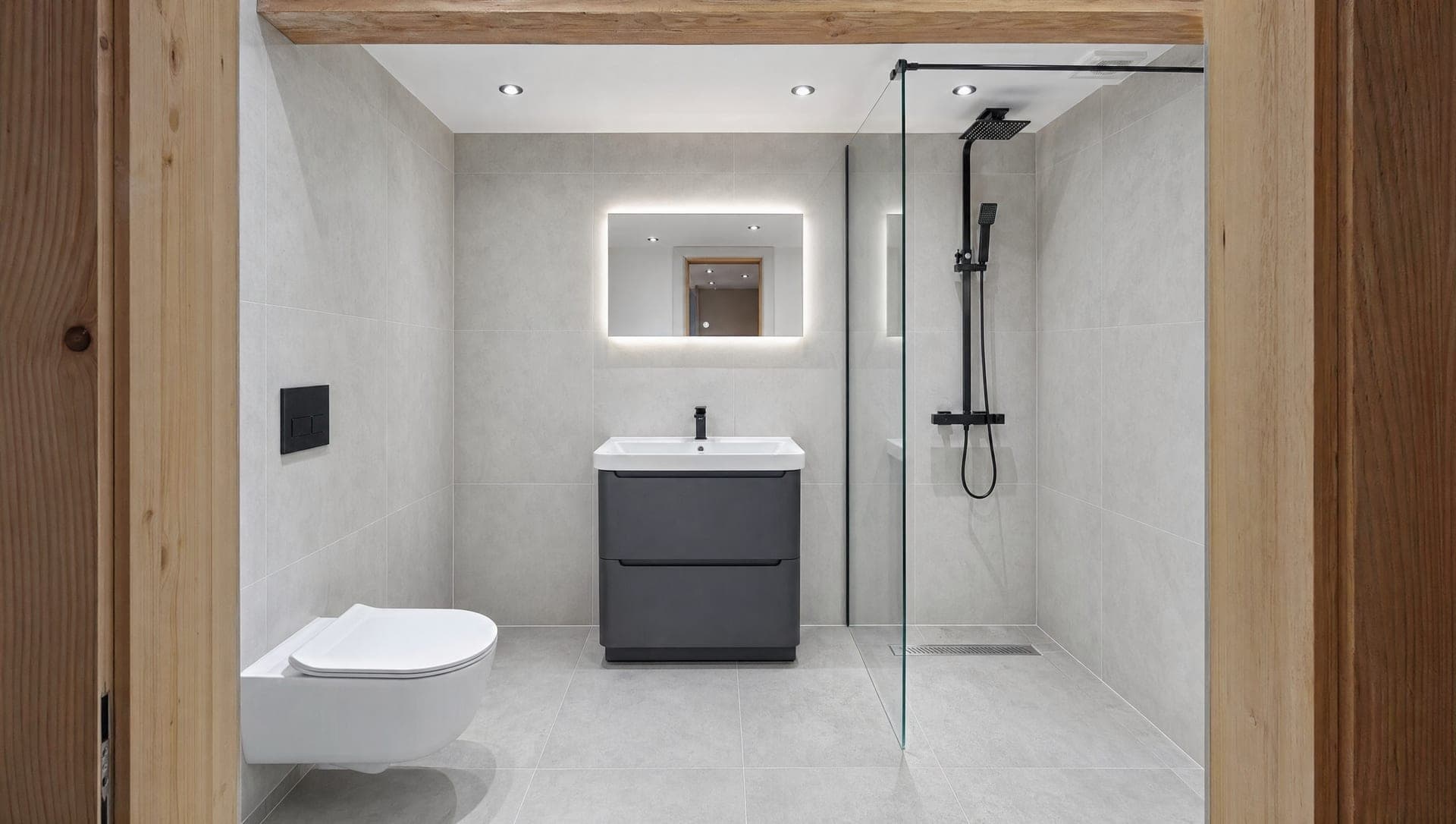Modern grey-tiled bathroom with anthracite vanity, walk-in glass shower and black fittings