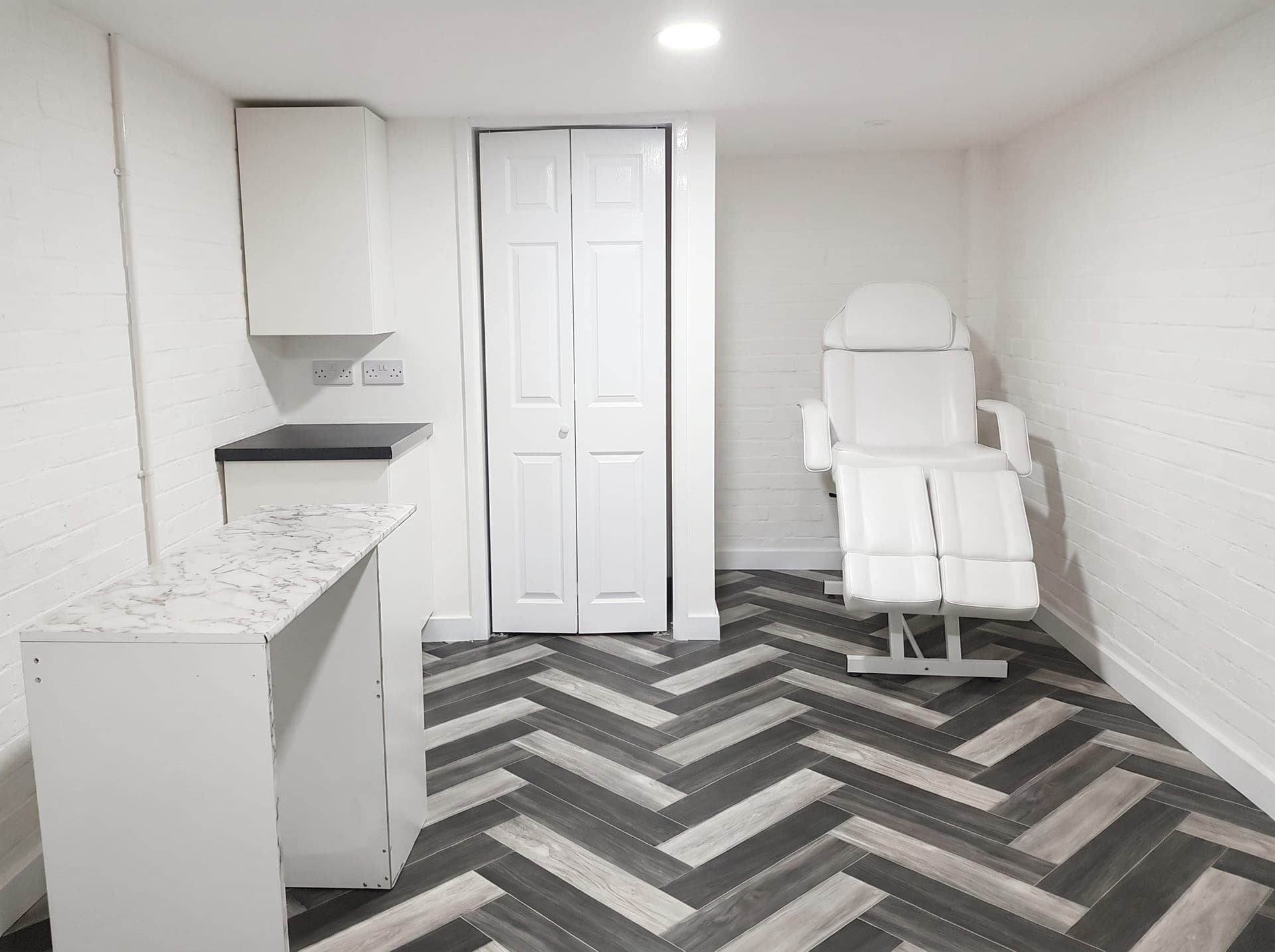 Finished aesthetics treatment room with a white treatment chair and herringbone vinyl flooring