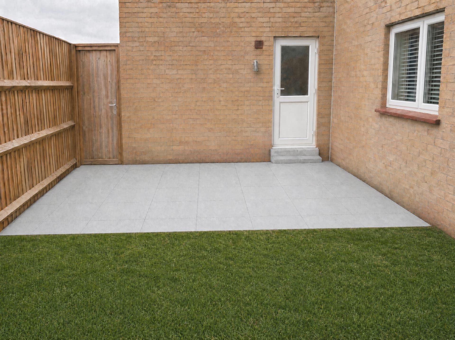 Grey porcelain patio with a white pebble drainage strip and an artificial grass lawn alongside