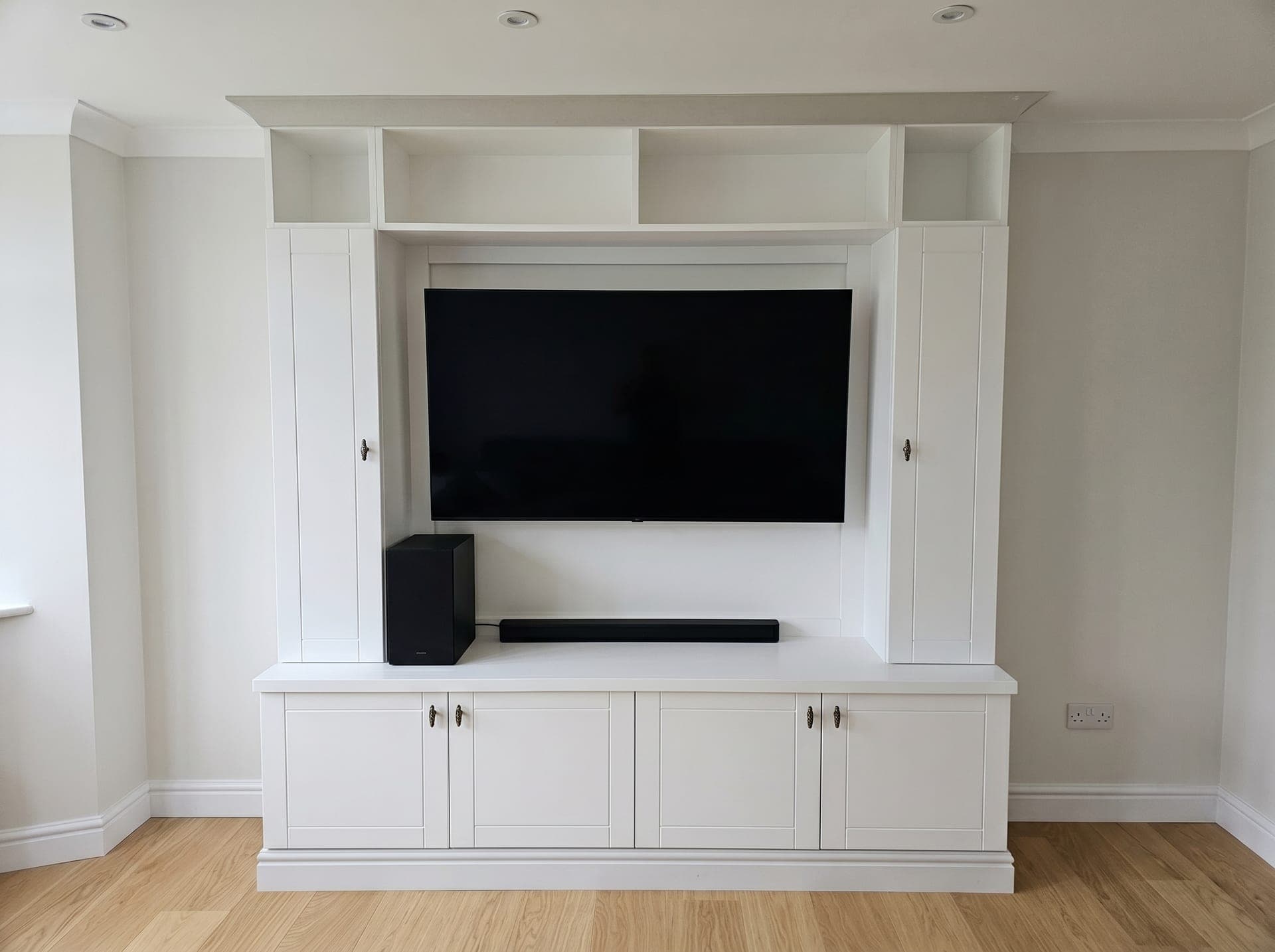 Bespoke fitted media wall in white with a wall-mounted television, soundbar, integrated cupboards and oak flooring