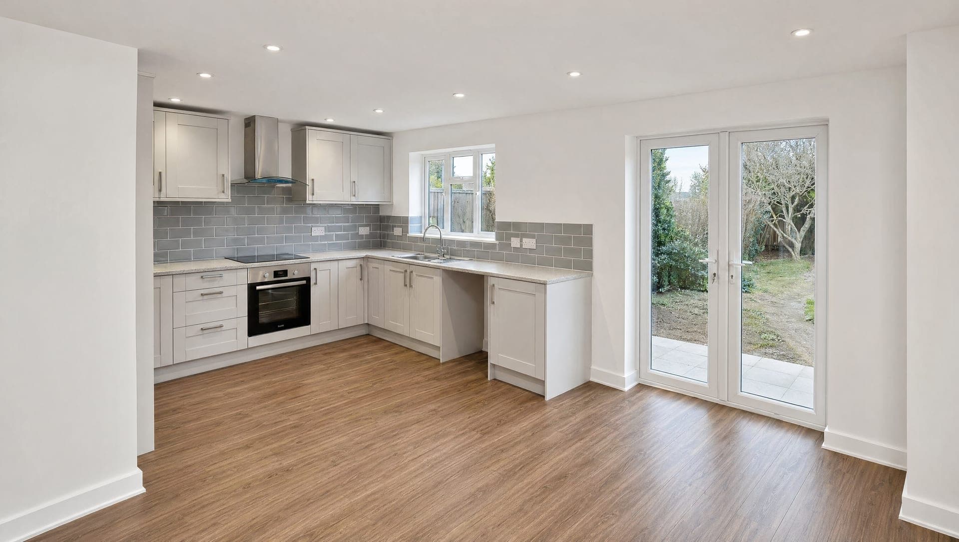 U-shape grey shaker kitchen with metro tile splashback, integrated oven and French doors out to the garden