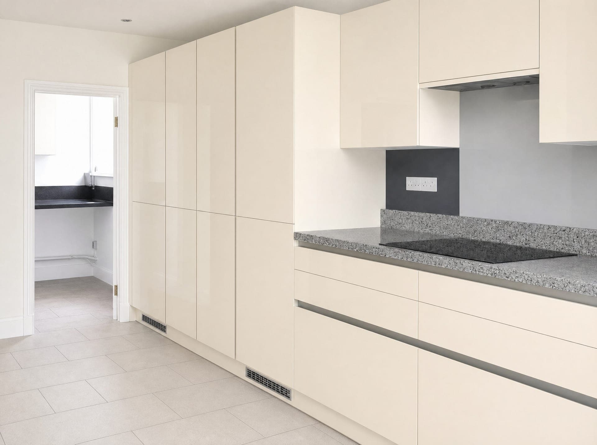 Handleless cream high-gloss kitchen with a dark stone worktop, induction hob and large floor tiles
